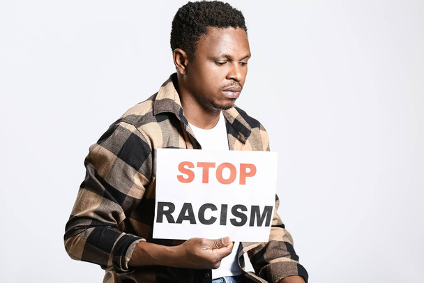 光の背景にポスターを持つ悲しいアフリカ系アメリカ人の男.人種差別をやめ - 写真・画像