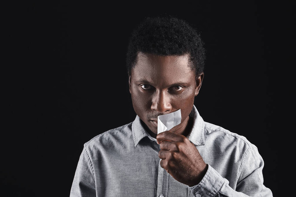 Sad African-American man removing tape from mouth on dark background. Stop racism - Photo, Image