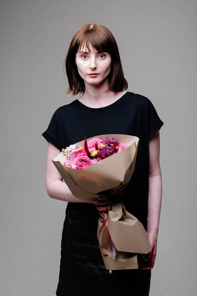 Portrait of young female florist with bouquet of flowers in beige package in the hands. Rosa spray, dahlia, celosia, matthiola, carnation. - Фото, изображение