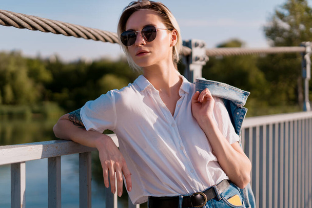 La mujer a la moda en las gafas de sol sobre el descanso en el puente
 - Foto, Imagen