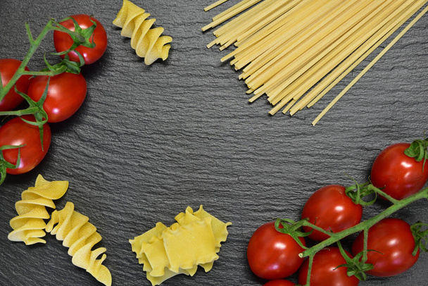 Background and frame with text field made of different pasta like spaghetti and spiral noodles with fresh tomatoes on a slate plate - Photo, image