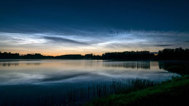 красивый ночной пейзаж с белыми серебряными облаками над озером, размытый передний план, очаровательные отражения облаков в озере воды, летняя ночь - Фото, изображение