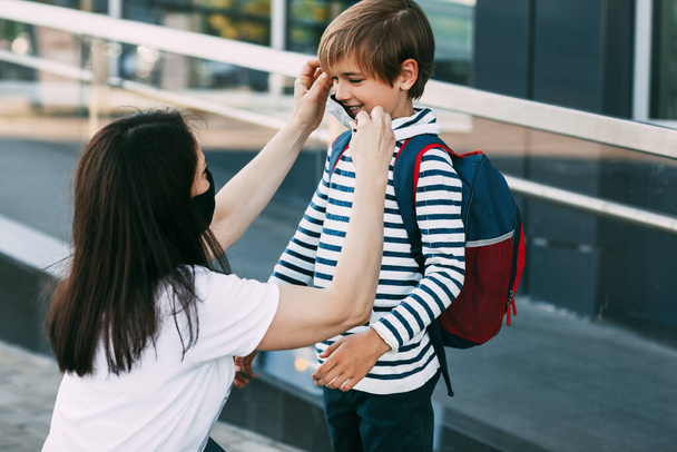 Anya beállítja a fia maszkját. Egy anya és egy gyermek útban az iskolába vagy óvodába egy koronavírus-világjárvány idején. Védőmaszk mint betegségmegelőzés - Fotó, kép