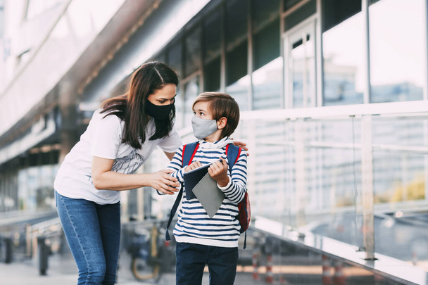 Un niño enmascarado sostiene una tableta mientras su madre lo ayuda a ponerse su mochila. Una madre acompaña a su hijo a la escuela durante la pandemia del coronavirus
 - Foto, Imagen