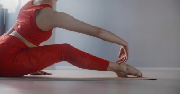 Молода жінка в червоному костюмі сидить на килимку для йоги і схиляється вперед до її ніг, людина займається фізичною підготовкою, розтягуванням йоги та гімнастикою, 4k 120p Пропонує 10 біт
 - Кадри, відео