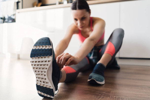 Kobieta wiąże buty sportowe siedząc na podłodze - Zdjęcie, obraz