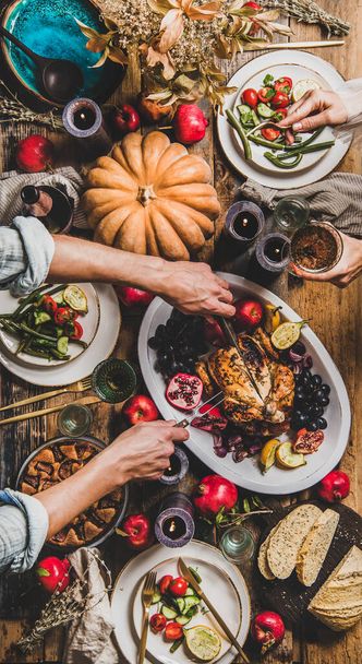 Thanksgiving party table setting. Flat-lay of people eating and celebrating holiday at table with roasted chicken, vegetables, fig pie, fruit, candles, tableware over wooden table background, top view - Φωτογραφία, εικόνα