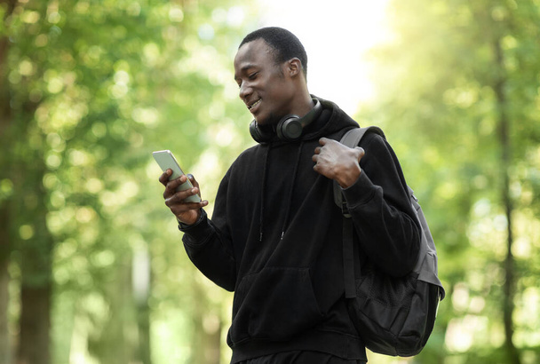Onnellinen afrikkalainen kaveri käyttää älypuhelinta, koulutus puistossa - Valokuva, kuva