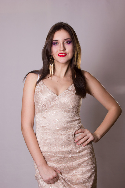 Studio portrait of a beautiful and sexy young brunette woman in evening beige lace dress and long gold earrings - Fotografie, Obrázek