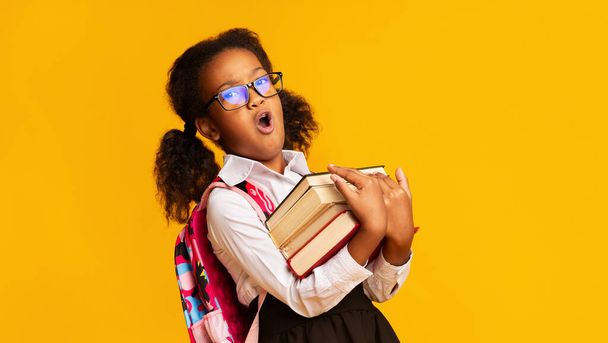 Fekete iskoláslány ásítás gazdaság könyvek pózol sárga háttér, panoráma - Fotó, kép