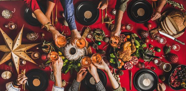 Family celebration Christmas, New Year. Flat-lay of people clinking glasses with champagne over table with red cloth with roasted turkey, bundt cake, fruit, decorations, top view, wide composition - Fotoğraf, Görsel
