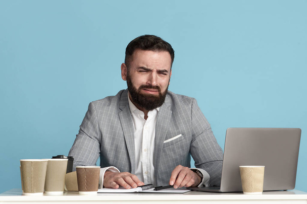 Millennial office employee whining or crying at desk because of too much work, blue background - Photo, Image