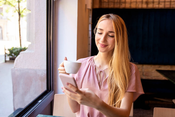 Tiro de mensagens de texto jovem mulher e desfrutar de uma xícara de café em um dia feliz no café
.  - Foto, Imagem