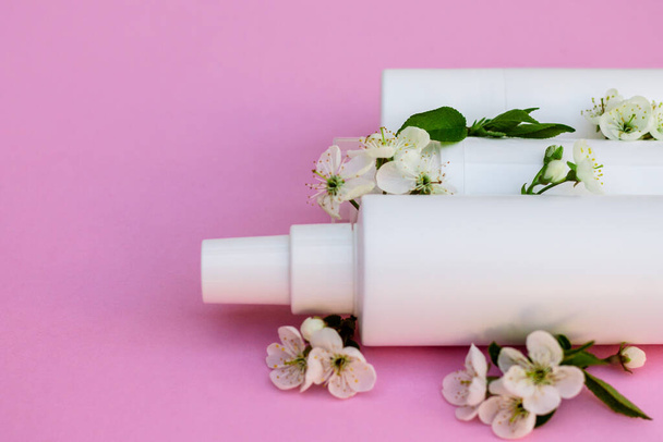 White cosmetic bottles, bath bomb, handmade soap, bath salt, massage brush, sponge, cotton buds with cherry flowers on a pink background. Natural organic cosmetics concept. - Photo, Image