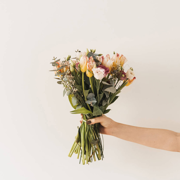 Female hand holding tulip flowers bouquet against white wall. Holiday celebration festive floral concept - Фото, зображення