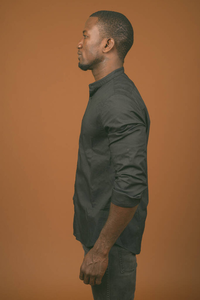 Студия фотографии красивого африканского бизнесмена в черной рубашке на коричневом фоне - Фото, изображение