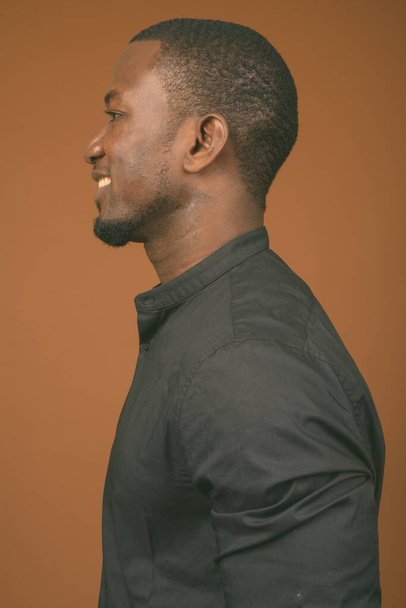 Studio shot of handsome African businessman wearing black shirt against brown background - Фото, зображення