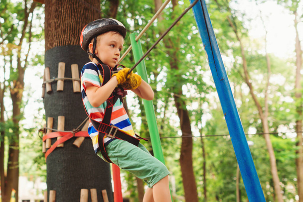 Little boy in the rope park pass obstacles. Cute kid climb the rope road. Adventure climbing high wire park. Boy wearing helmet and safety equipment. Extreme sport in adventure park. - Φωτογραφία, εικόνα