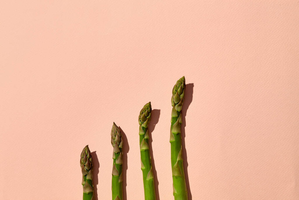 Ripe green asparagus stalks on pink background. Healthy nutrition, food and seasonal vegetables harvest. Close up, flat lay, top view - Photo, image
