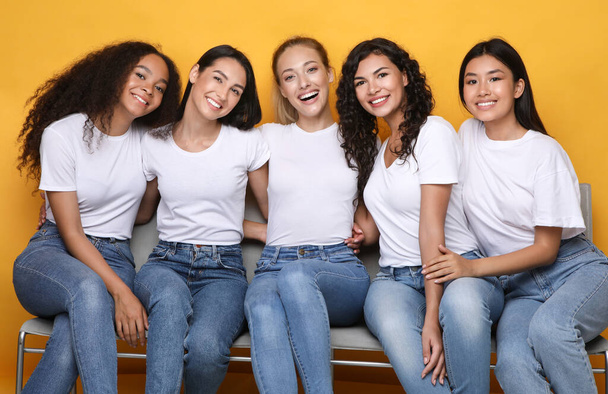 Iloiset tytöt Ystävät halaavat istuen penkillä keltaisella taustalla - Valokuva, kuva