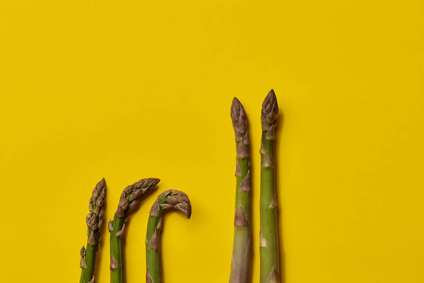 Raw green asparagus spears on yellow background. Healthy nutrition, food and seasonal vegetables harvest. Close up, flat lay, top view - 写真・画像