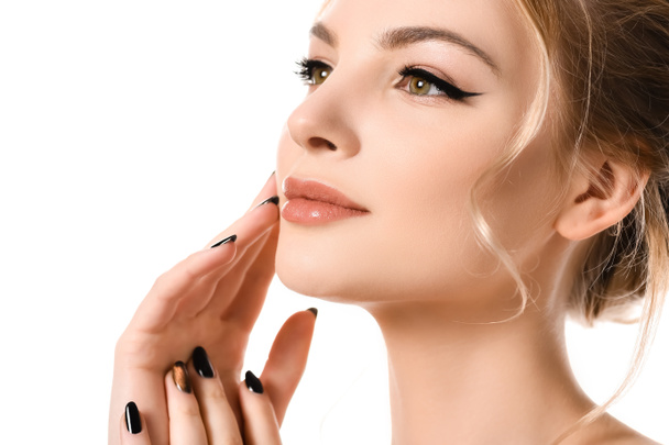 mooie blonde vrouw met make-up en zwarte nagels aanraken gezicht geïsoleerd op wit - Foto, afbeelding