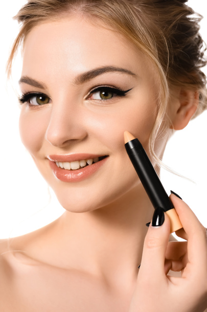 χαμογελαστή γυμνή όμορφη ξανθιά γυναίκα με μακιγιάζ και μαύρα νύχια εφαρμογή ραβδί concealer απομονώνονται σε λευκό - Φωτογραφία, εικόνα