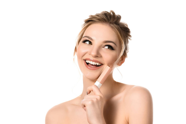 sonriente mujer rubia hermosa desnuda con maquillaje y uñas negras sosteniendo brillo de labios beige aislado en blanco
 - Foto, Imagen