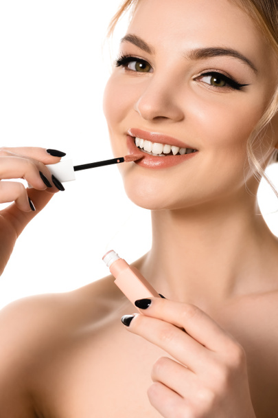 smiling naked beautiful blonde woman with makeup and black nails applying beige lip gloss isolated on white - Фото, изображение