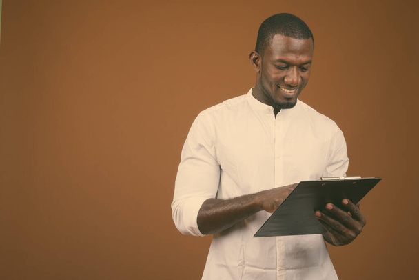 Studioaufnahme eines gut aussehenden afrikanischen Geschäftsmannes im weißen Hemd vor braunem Hintergrund - Foto, Bild