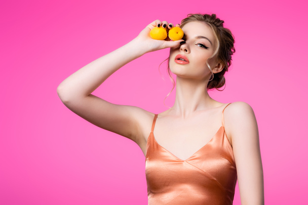 elegant beautiful blonde woman in silk dress holding apricots isolated on pink - Фото, изображение