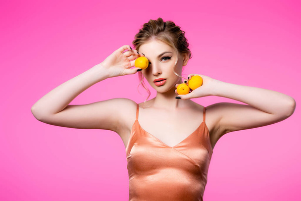 elegant beautiful blonde woman in silk dress holding apricots isolated on pink - Фото, зображення