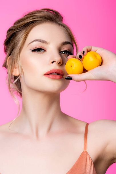 elegant beautiful blonde woman holding apricots isolated on pink - Foto, afbeelding