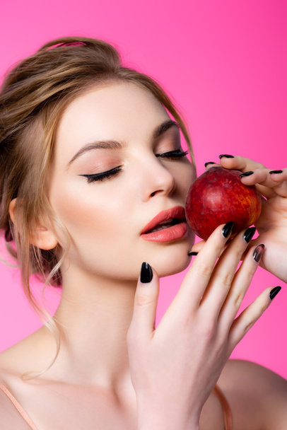 elegant beautiful blonde woman with closed eyes holding peach isolated on pink - 写真・画像