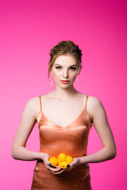 elegant beautiful blonde woman in silk dress holding ripe apricots isolated on pink - Foto, afbeelding