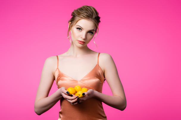 tyylikäs kaunis blondi nainen silkki mekko tilalla kypsä aprikoosit eristetty vaaleanpunainen - Valokuva, kuva