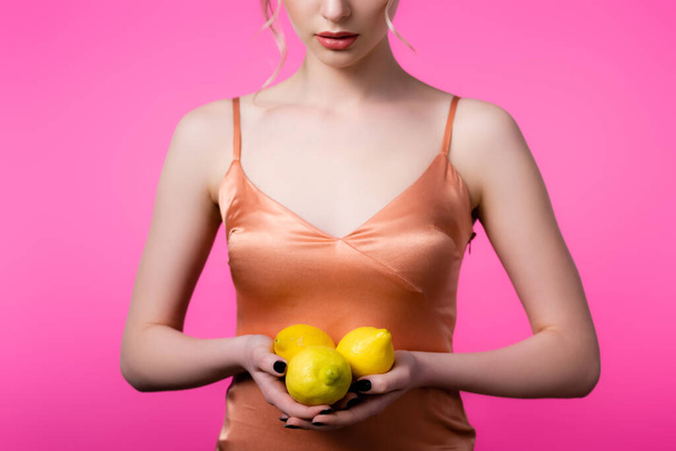 cropped view of elegant beautiful woman holding ripe lemons isolated on pink - Photo, image