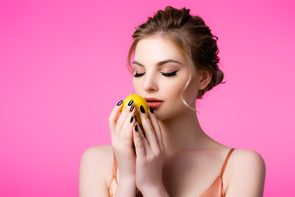 elegant beautiful blonde woman with closed eyes holding ripe lemon isolated on pink - 写真・画像