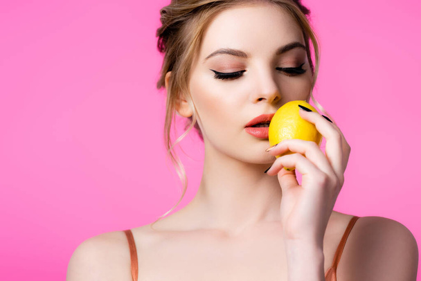 elegant beautiful blonde woman holding ripe lemon near lips isolated on pink - Photo, Image