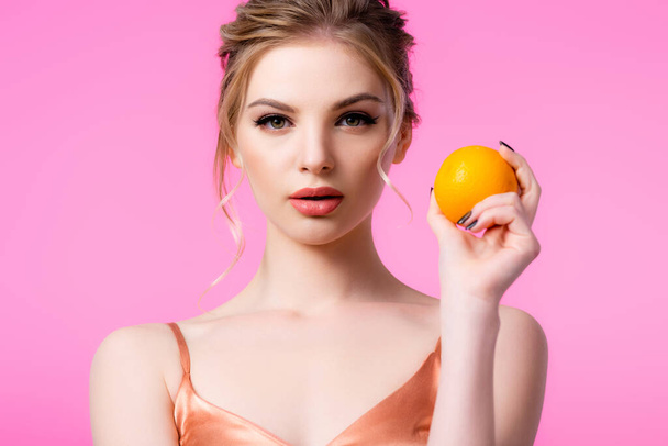elegant beautiful blonde woman holding ripe orange isolated on pink - Valokuva, kuva