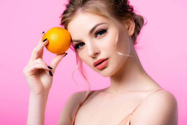 elegant beautiful blonde woman holding ripe orange isolated on pink - Photo, Image
