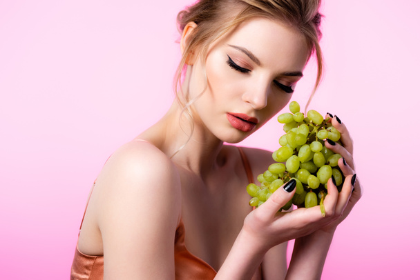 elegant beautiful blonde woman holding green grapes isolated on pink - 写真・画像