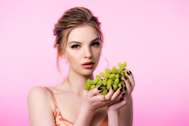 elegant beautiful blonde woman holding green grapes isolated on pink - Foto, Bild