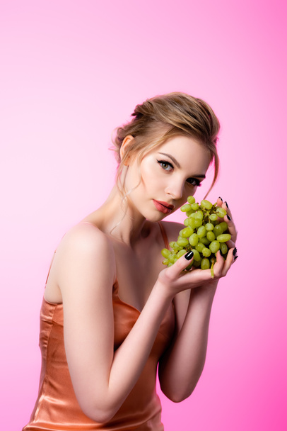 elegant beautiful blonde woman holding green grapes isolated on pink - Photo, Image