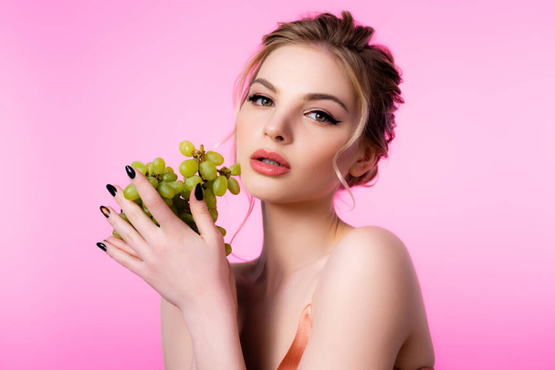 elegant beautiful blonde woman holding green grapes isolated on pink - Фото, зображення