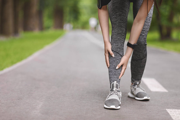 Joven corredora que sufre de férulas en la espinilla mientras trota en el parque
 - Foto, imagen