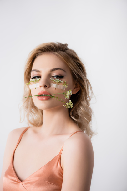 beautiful blonde woman in silk dress with wildflowers under eyes and in mouth isolated on white - Foto, immagini