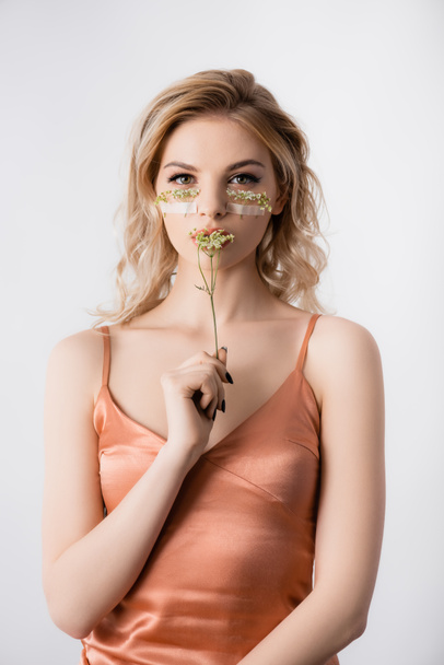 hermosa mujer rubia en vestido de seda con flores silvestres bajo los ojos y cerca de la boca aislada en blanco
 - Foto, imagen