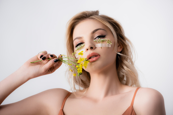 beautiful blonde woman with wildflowers under eyes and near mouth isolated on white - Φωτογραφία, εικόνα