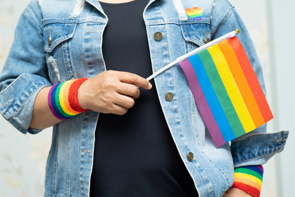 Dame asiatique portant une veste en jean bleu ou une chemise en denim et tenant un drapeau de couleur arc-en-ciel, symbole du mois de la fierté LGBT, célèbre chaque année en juin les droits humains des homosexuels, lesbiennes, bisexuels, transgenres. - Photo, image